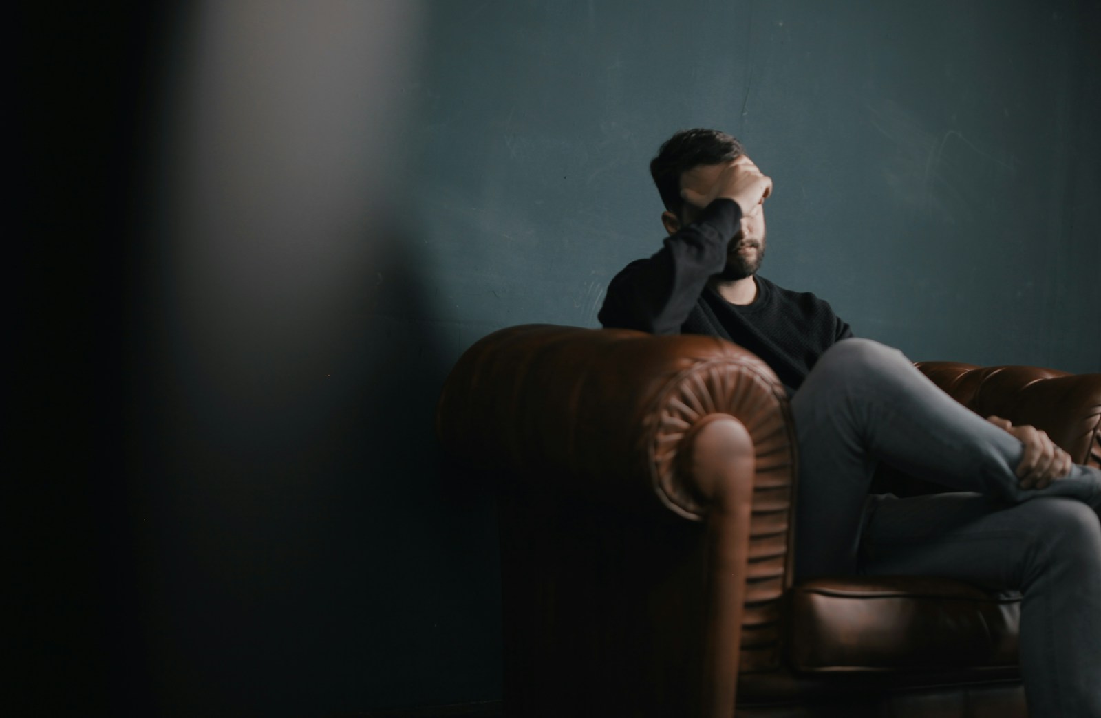 a man holds his head while sitting on a sofa dealing with grief & loss