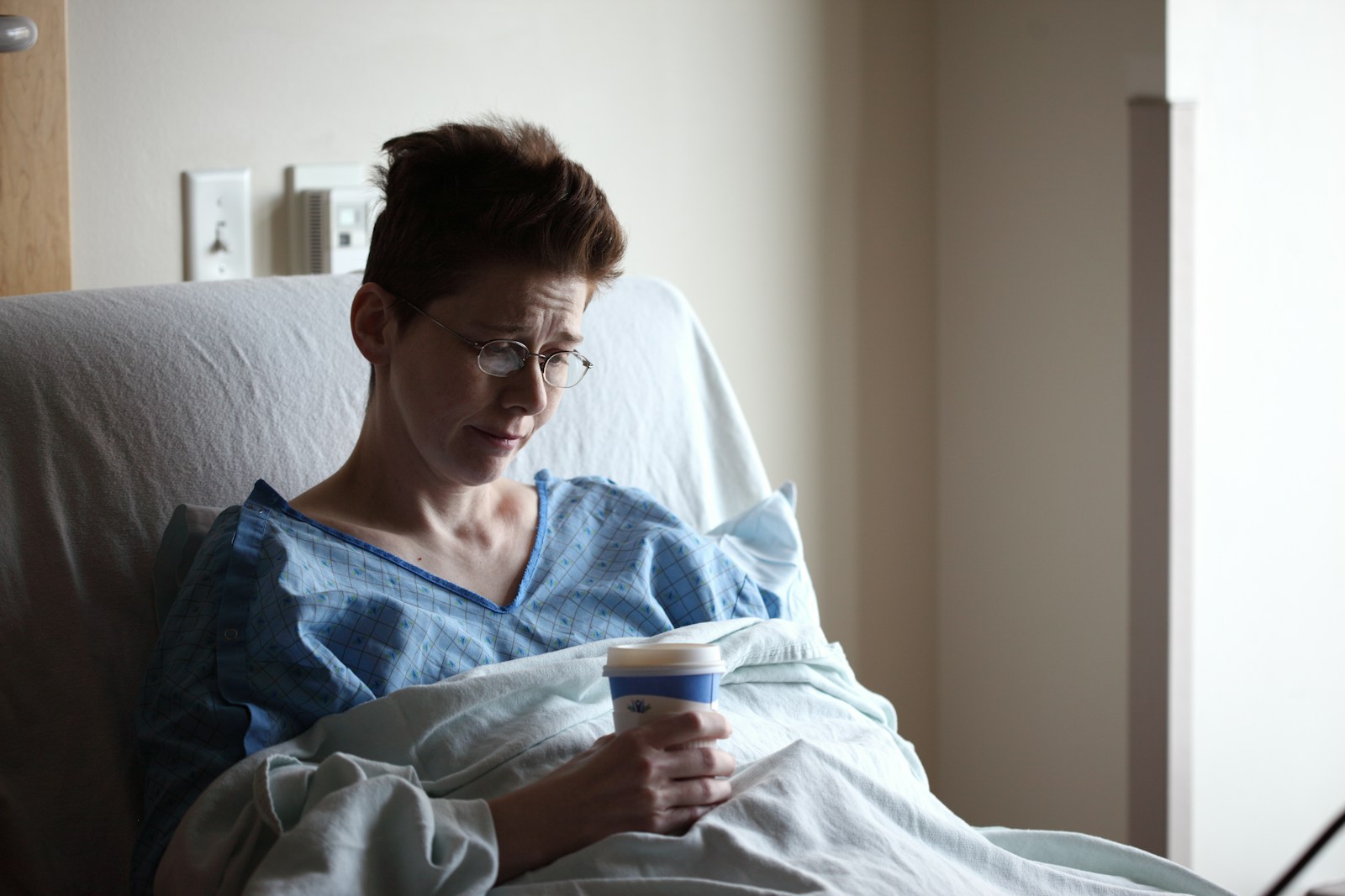 woman on bed holding plastic cup dealing with chronic illness