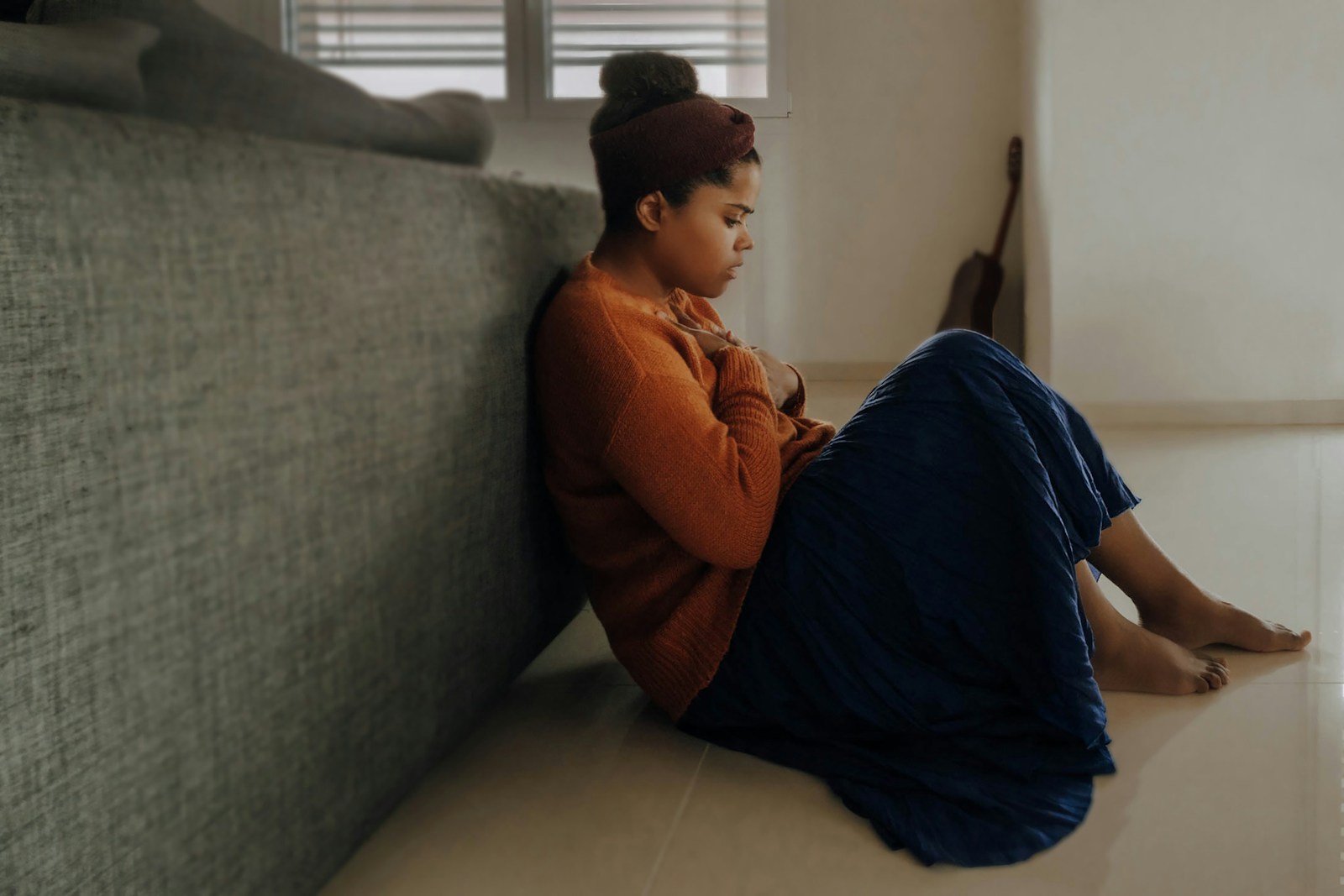 person in orange long sleeve shirt sitting next to gray couch dealing with anxiety and depression