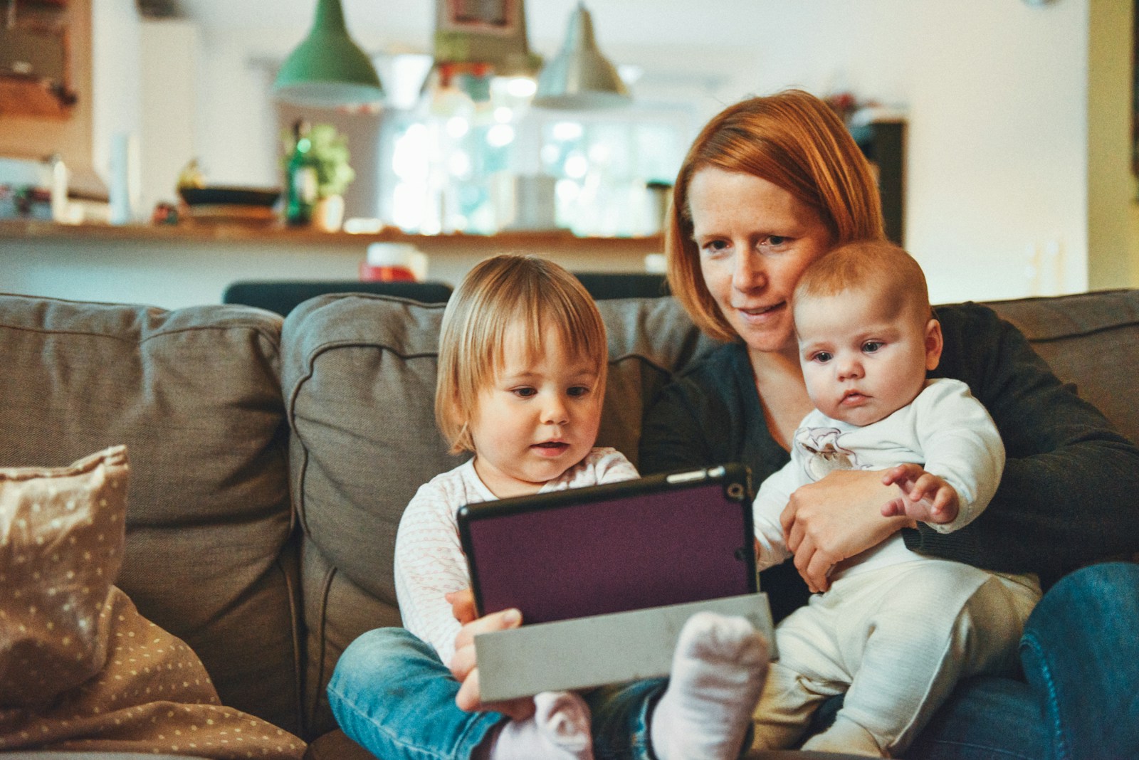 two babies and woman sitting on sofa while holding baby and watching on tablet representative of perinatal mental health