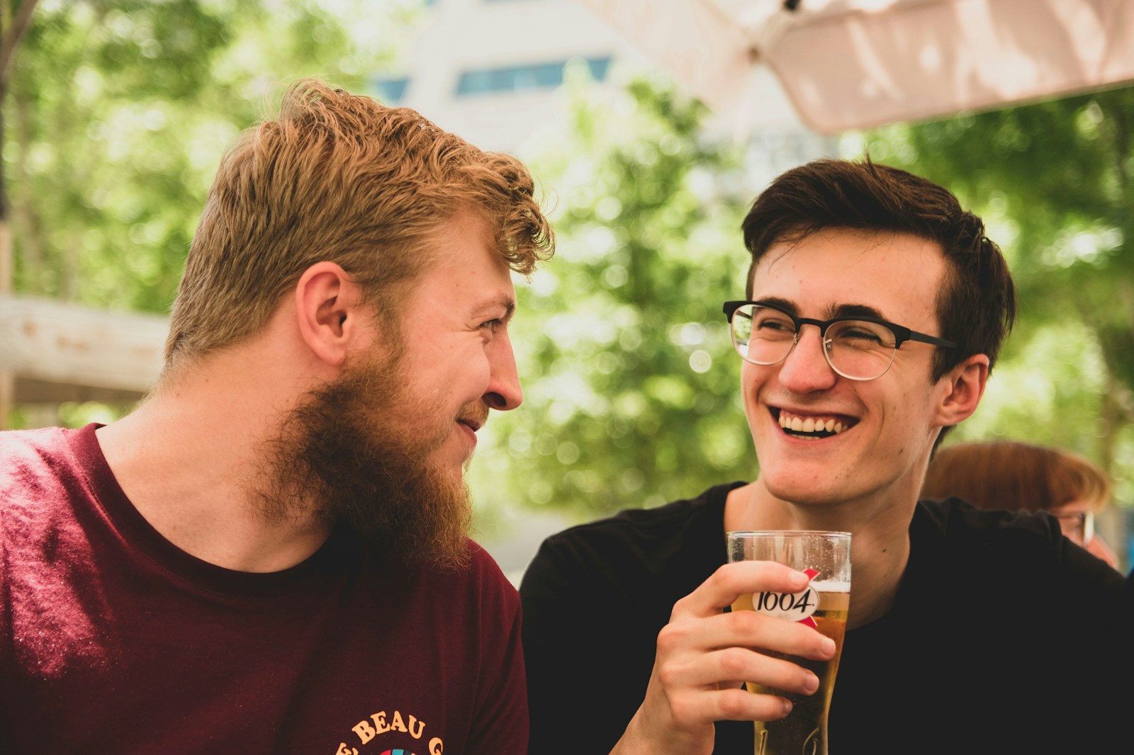 two men smiling near trees, representing happiness in a non-monogamous relationship