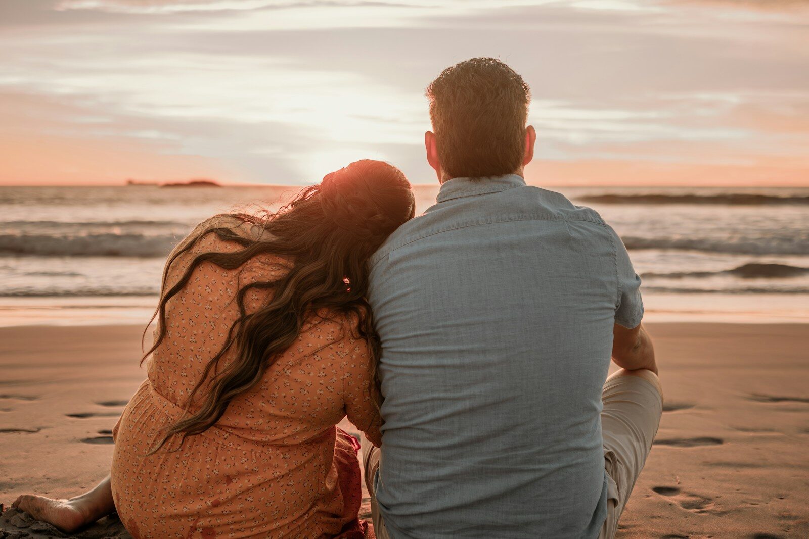 a man and woman sitting on the beach watching the sunset relaxed